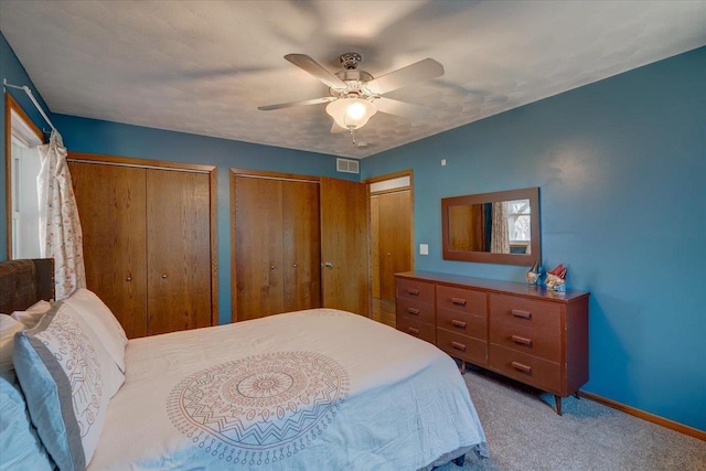 bedroom with two closets, ceiling fan, and carpet flooring