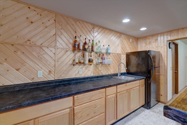 bar featuring sink, wooden walls, black fridge, and light brown cabinets