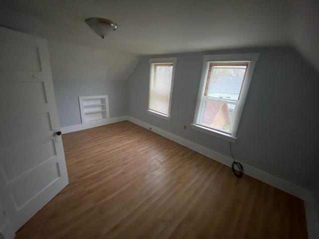 additional living space featuring wood-type flooring, vaulted ceiling, and built in features