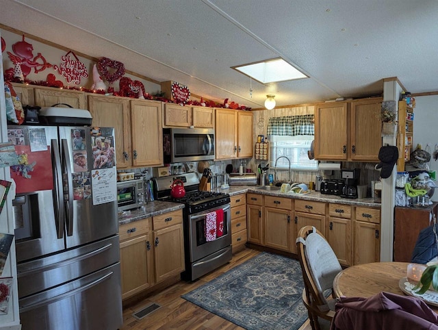 kitchen featuring sink, dark wood-type flooring, appliances with stainless steel finishes, lofted ceiling with skylight, and light stone counters