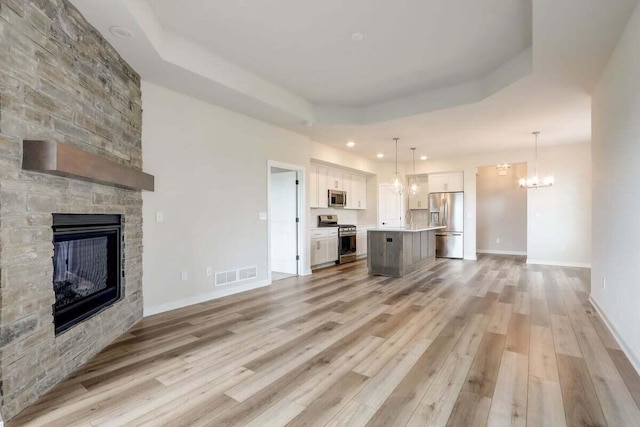 unfurnished living room with a tray ceiling, a stone fireplace, light hardwood / wood-style flooring, and a notable chandelier