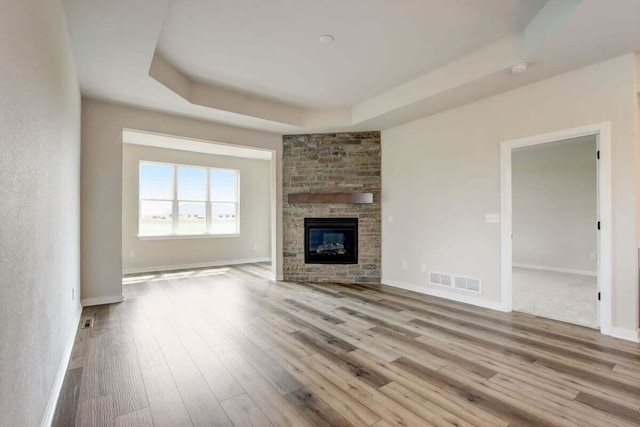 unfurnished living room with a fireplace, a raised ceiling, and light hardwood / wood-style flooring