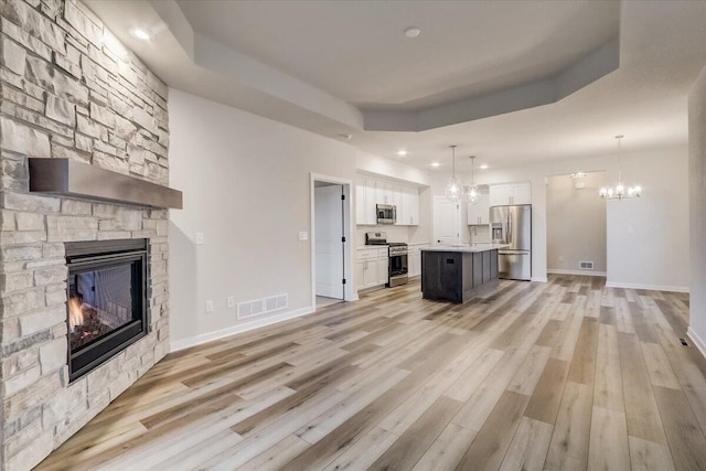 unfurnished living room with light hardwood / wood-style floors, a notable chandelier, a fireplace, and a tray ceiling