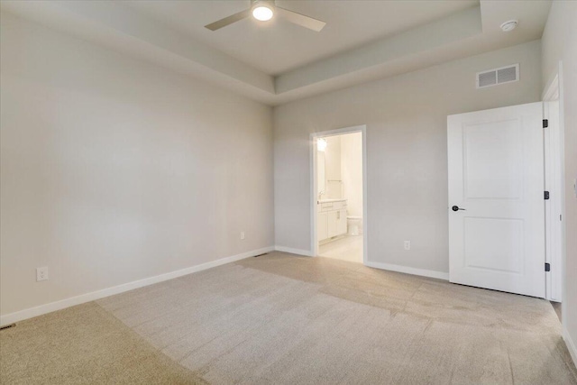 unfurnished bedroom featuring ensuite bathroom, light carpet, ceiling fan, and a tray ceiling