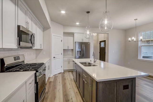 kitchen featuring white cabinetry, decorative light fixtures, appliances with stainless steel finishes, an island with sink, and light hardwood / wood-style floors