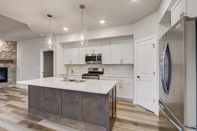 kitchen with a center island with sink, appliances with stainless steel finishes, pendant lighting, and white cabinets