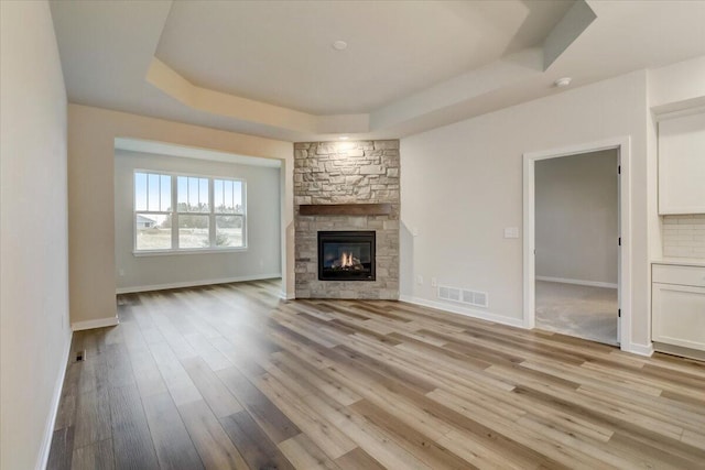 unfurnished living room featuring a stone fireplace, light hardwood / wood-style flooring, and a tray ceiling