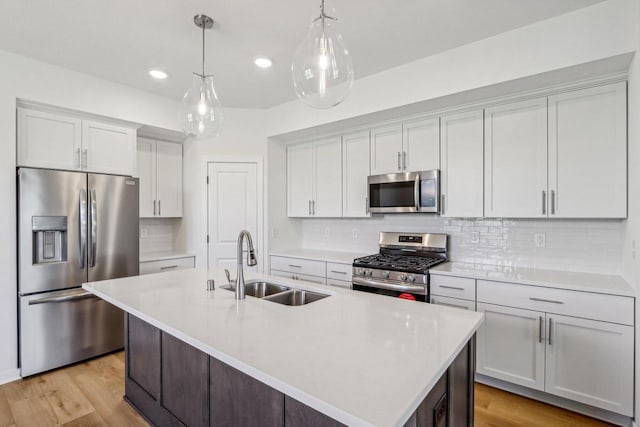 kitchen featuring stainless steel appliances, hanging light fixtures, sink, and a center island with sink