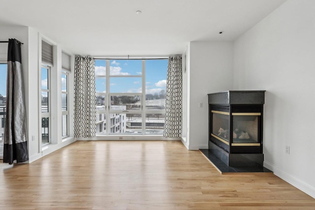 unfurnished living room with a multi sided fireplace, a wall of windows, and light wood-type flooring