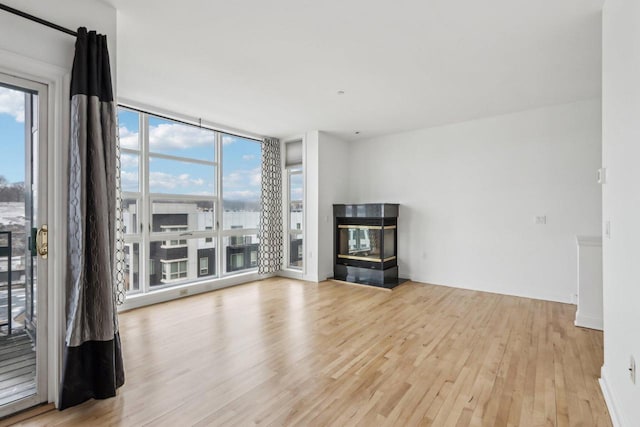 unfurnished living room featuring light hardwood / wood-style floors, floor to ceiling windows, a healthy amount of sunlight, and a multi sided fireplace