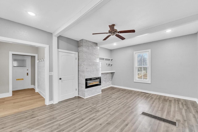 unfurnished living room featuring ceiling fan, a fireplace, beam ceiling, and light hardwood / wood-style flooring