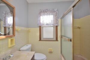 full bathroom with tile walls, vanity, bath / shower combo with glass door, and toilet