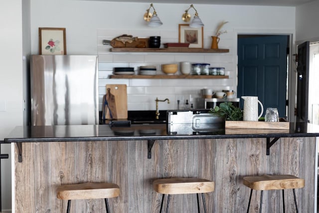 bar featuring backsplash and stainless steel refrigerator