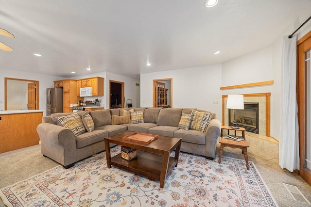 living room with a tile fireplace and light carpet