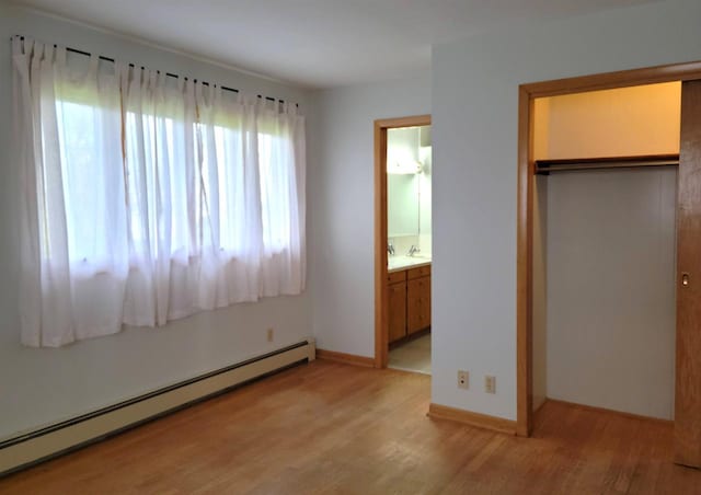 unfurnished bedroom featuring a closet, a baseboard heating unit, light wood-style floors, a sink, and baseboards