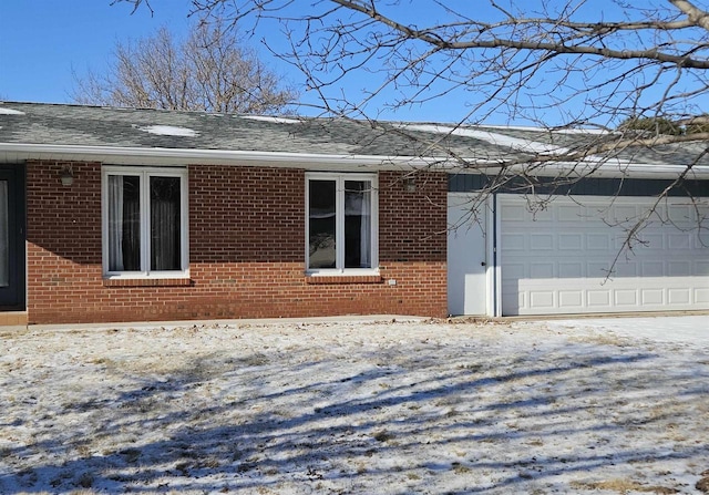 view of snowy exterior featuring a garage, a shingled roof, and brick siding