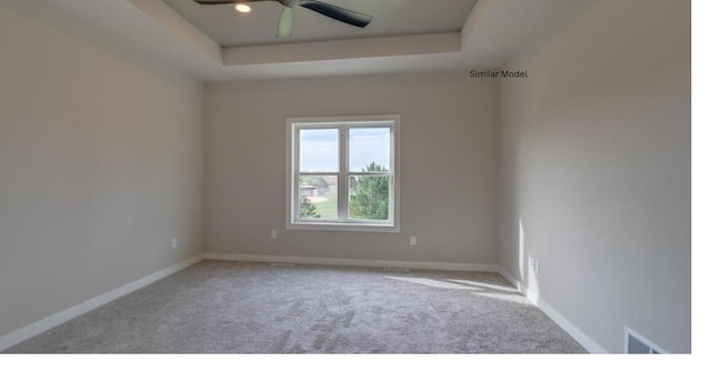 carpeted spare room with a tray ceiling and ceiling fan