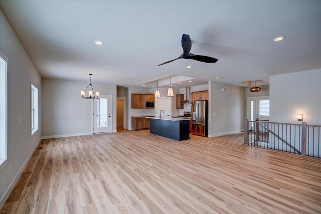 kitchen with hanging light fixtures, stainless steel fridge, an island with sink, ceiling fan with notable chandelier, and light hardwood / wood-style floors