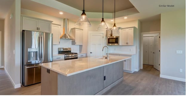 kitchen with a center island with sink, wall chimney range hood, decorative light fixtures, and appliances with stainless steel finishes