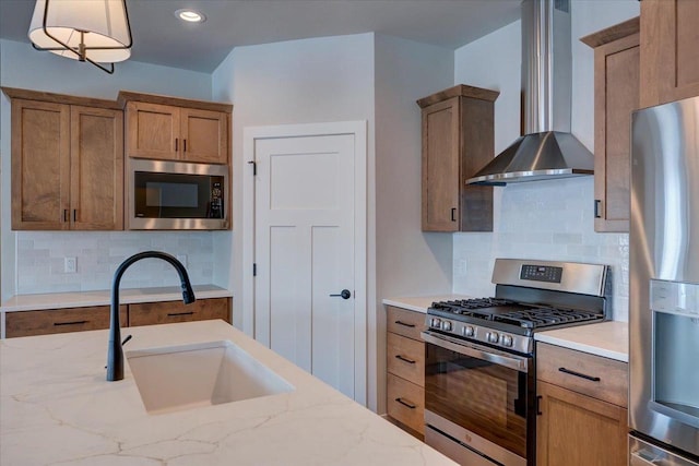 kitchen featuring sink, stainless steel appliances, pendant lighting, light stone counters, and wall chimney range hood