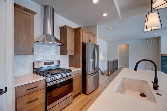 kitchen with sink, tasteful backsplash, appliances with stainless steel finishes, pendant lighting, and wall chimney range hood