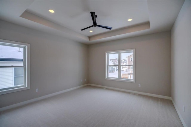 unfurnished room featuring a tray ceiling, ceiling fan, and light carpet