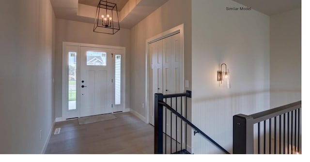 entryway featuring a raised ceiling, wood-type flooring, and a notable chandelier