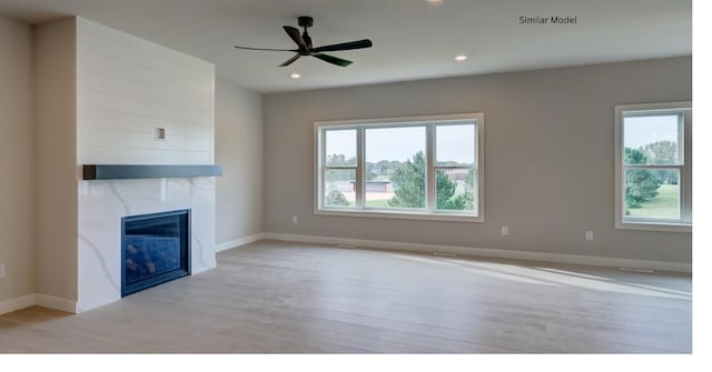 unfurnished living room featuring a high end fireplace, ceiling fan, plenty of natural light, and light hardwood / wood-style flooring