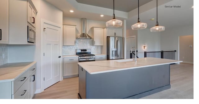 kitchen featuring light stone counters, decorative light fixtures, appliances with stainless steel finishes, an island with sink, and wall chimney exhaust hood