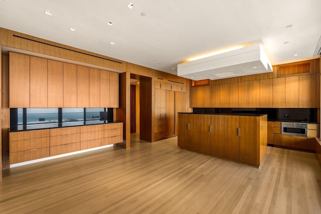 kitchen featuring wooden walls, a large island, light hardwood / wood-style floors, and stainless steel oven