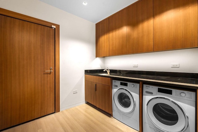 laundry room featuring cabinets, washing machine and clothes dryer, sink, and light hardwood / wood-style floors