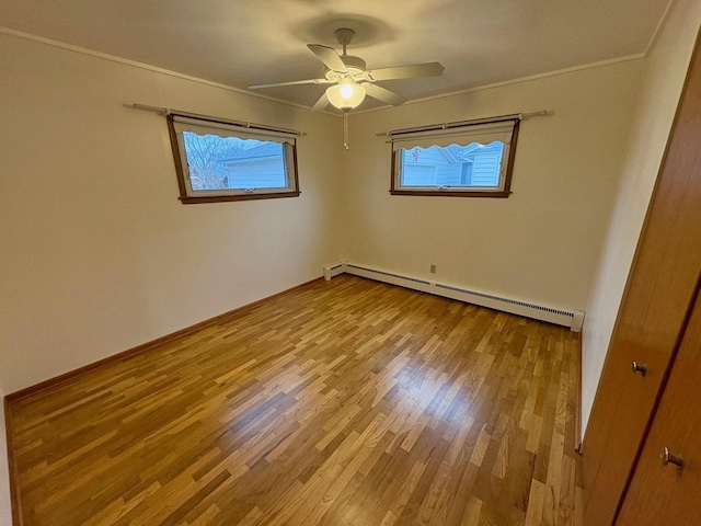 spare room featuring baseboard heating, ceiling fan, ornamental molding, and light hardwood / wood-style flooring