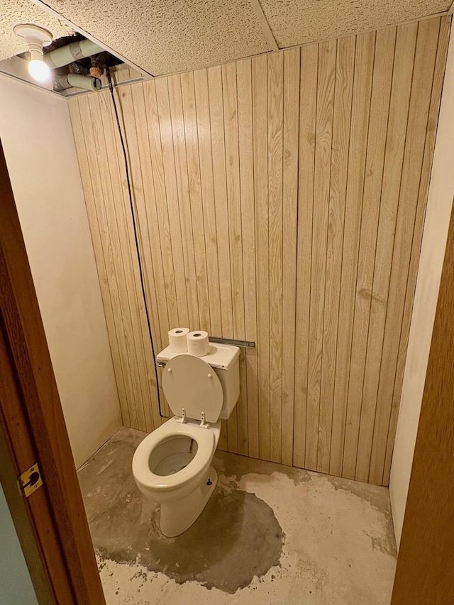 bathroom featuring concrete floors, toilet, and wood walls