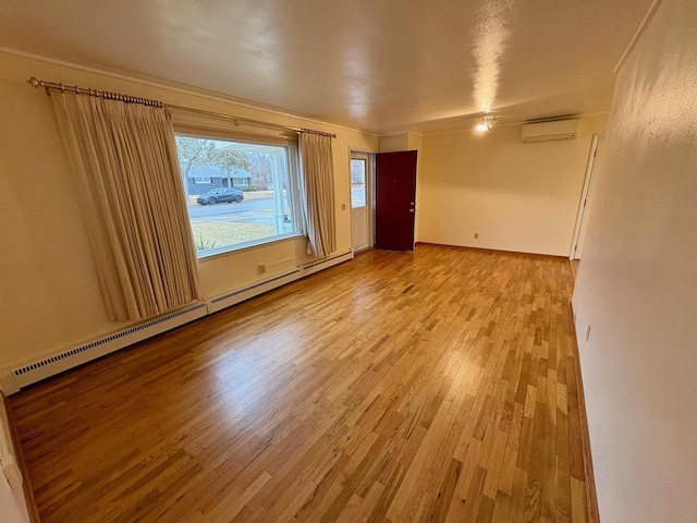 empty room with a wall mounted AC, baseboard heating, and light hardwood / wood-style floors