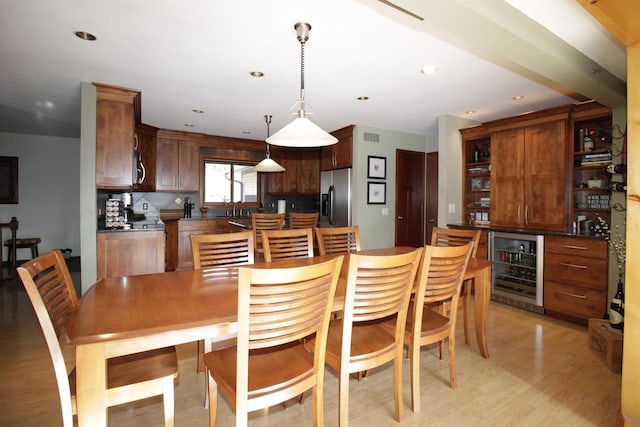 kitchen featuring pendant lighting, appliances with stainless steel finishes, tasteful backsplash, light hardwood / wood-style floors, and beverage cooler