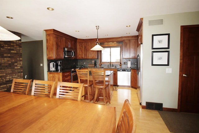 kitchen featuring decorative light fixtures, sink, backsplash, stainless steel appliances, and light hardwood / wood-style flooring