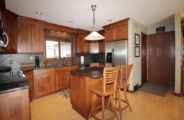 kitchen featuring sink, stainless steel fridge, backsplash, a kitchen island, and decorative light fixtures