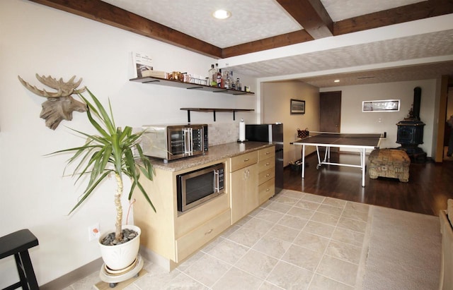 kitchen featuring stainless steel microwave, light brown cabinetry, light tile patterned floors, a textured ceiling, and beam ceiling