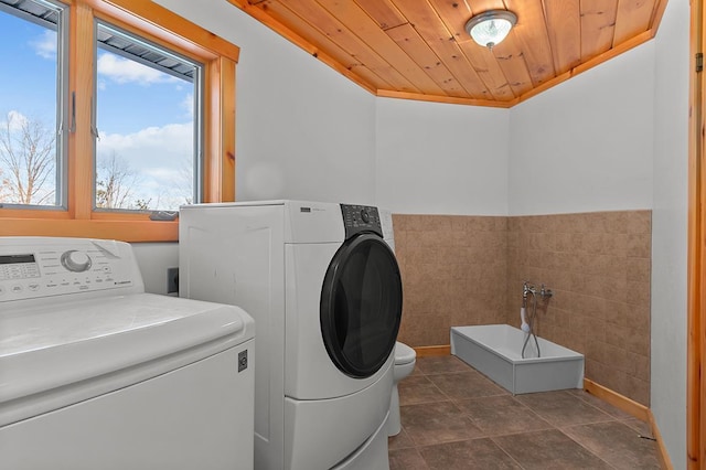 clothes washing area with separate washer and dryer, tile walls, dark tile patterned flooring, and wood ceiling