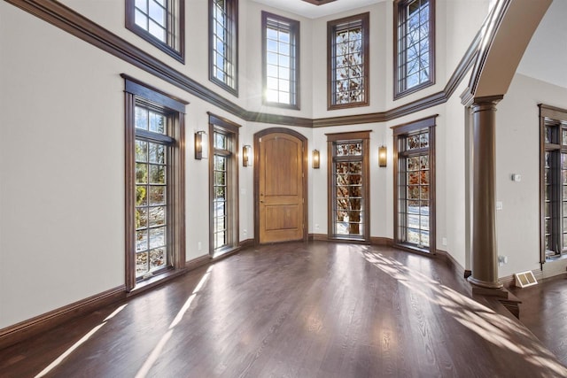 foyer entrance with decorative columns, a towering ceiling, a wealth of natural light, and dark wood-type flooring