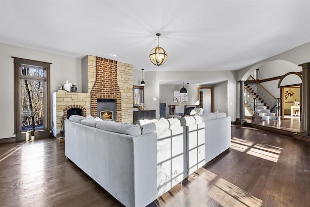 living room with dark wood-type flooring, an inviting chandelier, and decorative columns