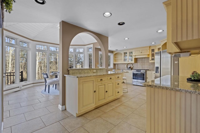 kitchen with light tile patterned flooring, a kitchen island, appliances with stainless steel finishes, tasteful backsplash, and light stone counters