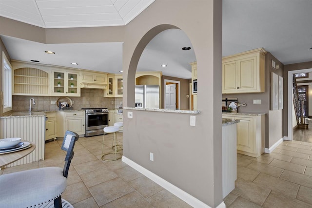 kitchen featuring a breakfast bar, light stone counters, crown molding, stainless steel appliances, and cream cabinetry