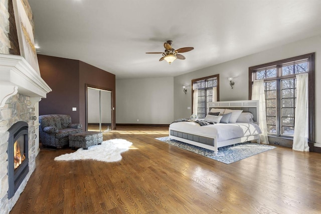 bedroom featuring wood-type flooring, a stone fireplace, and ceiling fan