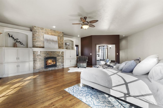 bedroom featuring ceiling fan, wood-type flooring, and a stone fireplace