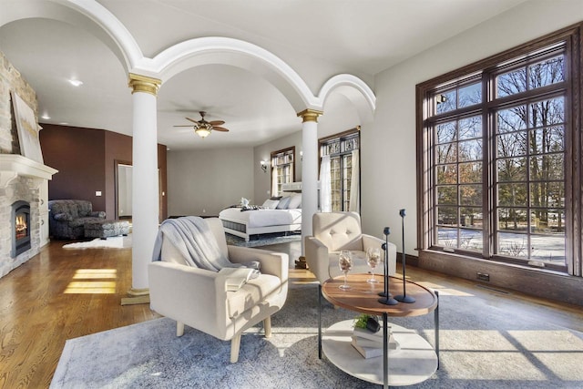 living room with decorative columns, ceiling fan, wood-type flooring, and a fireplace