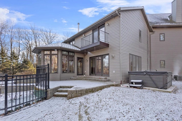 snow covered property with a hot tub, a balcony, and a sunroom