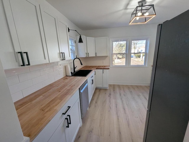 kitchen with appliances with stainless steel finishes, decorative light fixtures, butcher block counters, sink, and white cabinets