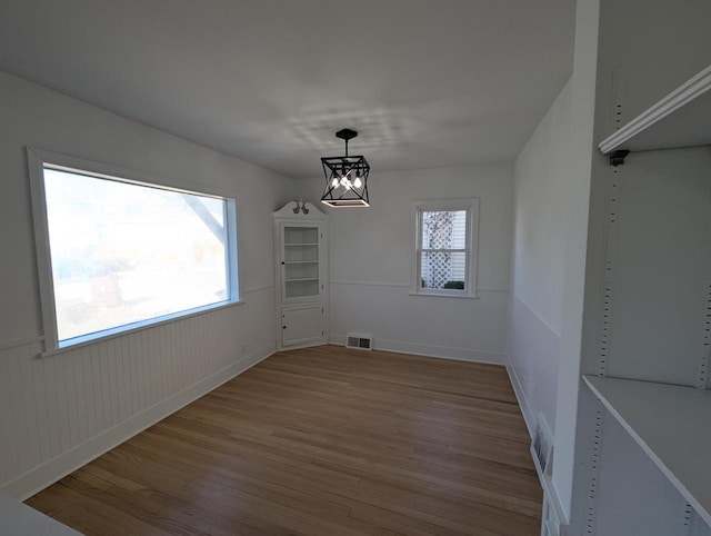 unfurnished dining area with wood-type flooring and a notable chandelier