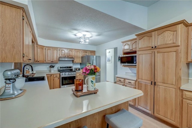 kitchen with sink, a breakfast bar, appliances with stainless steel finishes, a textured ceiling, and kitchen peninsula